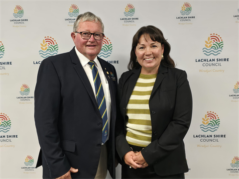 Smiling man and woman wearing suits standing in front of council logo