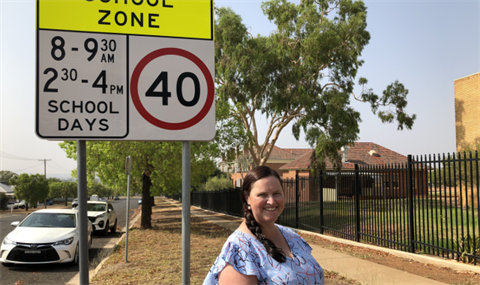 woman standing in front of school zone speed sign