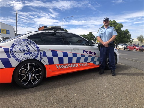 uniformed police officer standing in front of highway patrol car