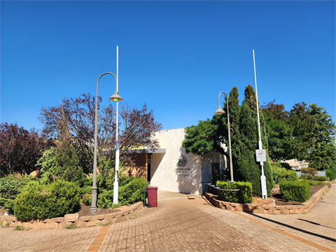 Picture of white building with flagpoles and shrubs in the foreground