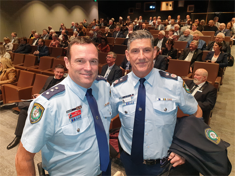 Two men in police uniform standing in front of crowd in auditorium